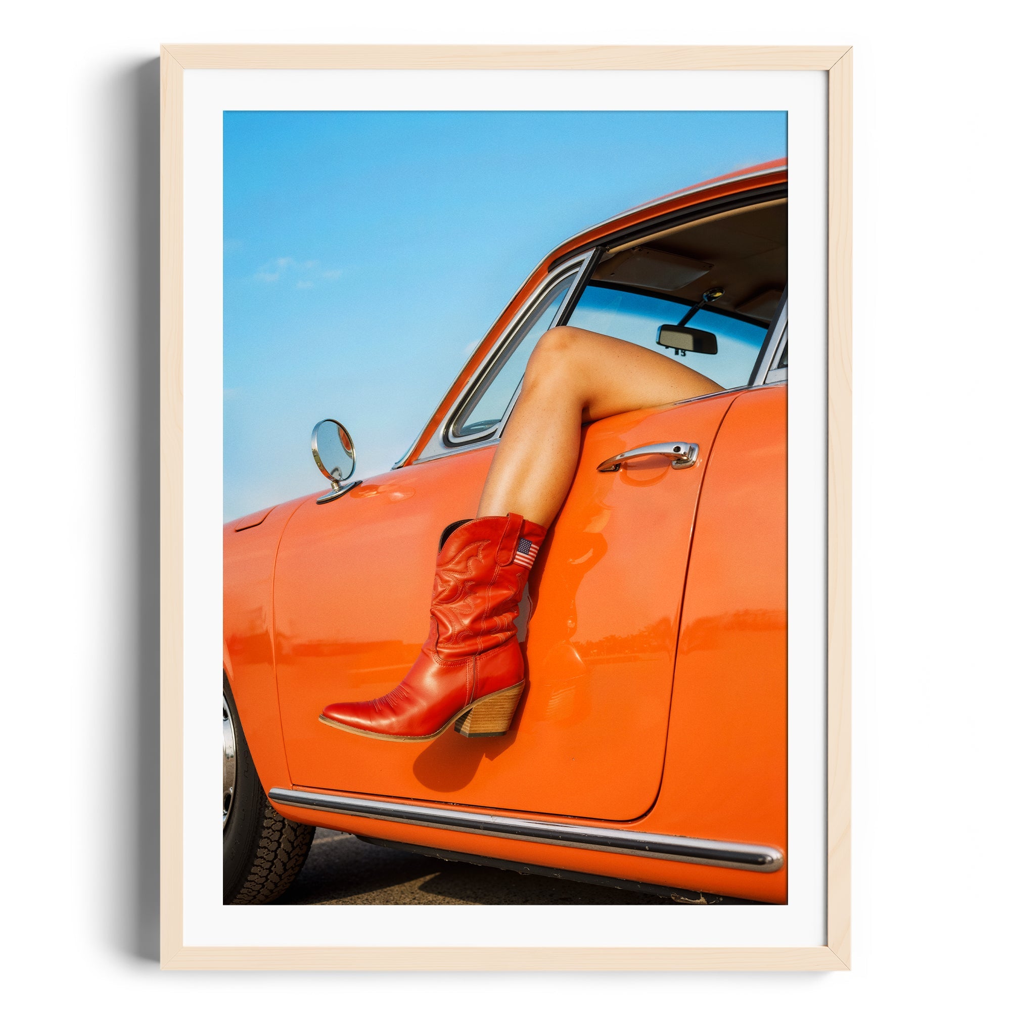 Red cowgirl boot resting on an orange car, showcasing vibrant colors in a fine art gallery display setting.
