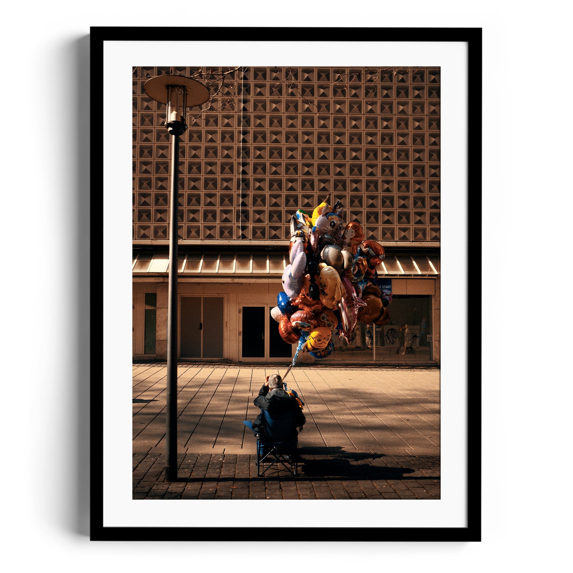 Man sitting under a streetlamp surrounded by colorful balloons in an urban setting, fine art photography by Marcelo Cadavid.