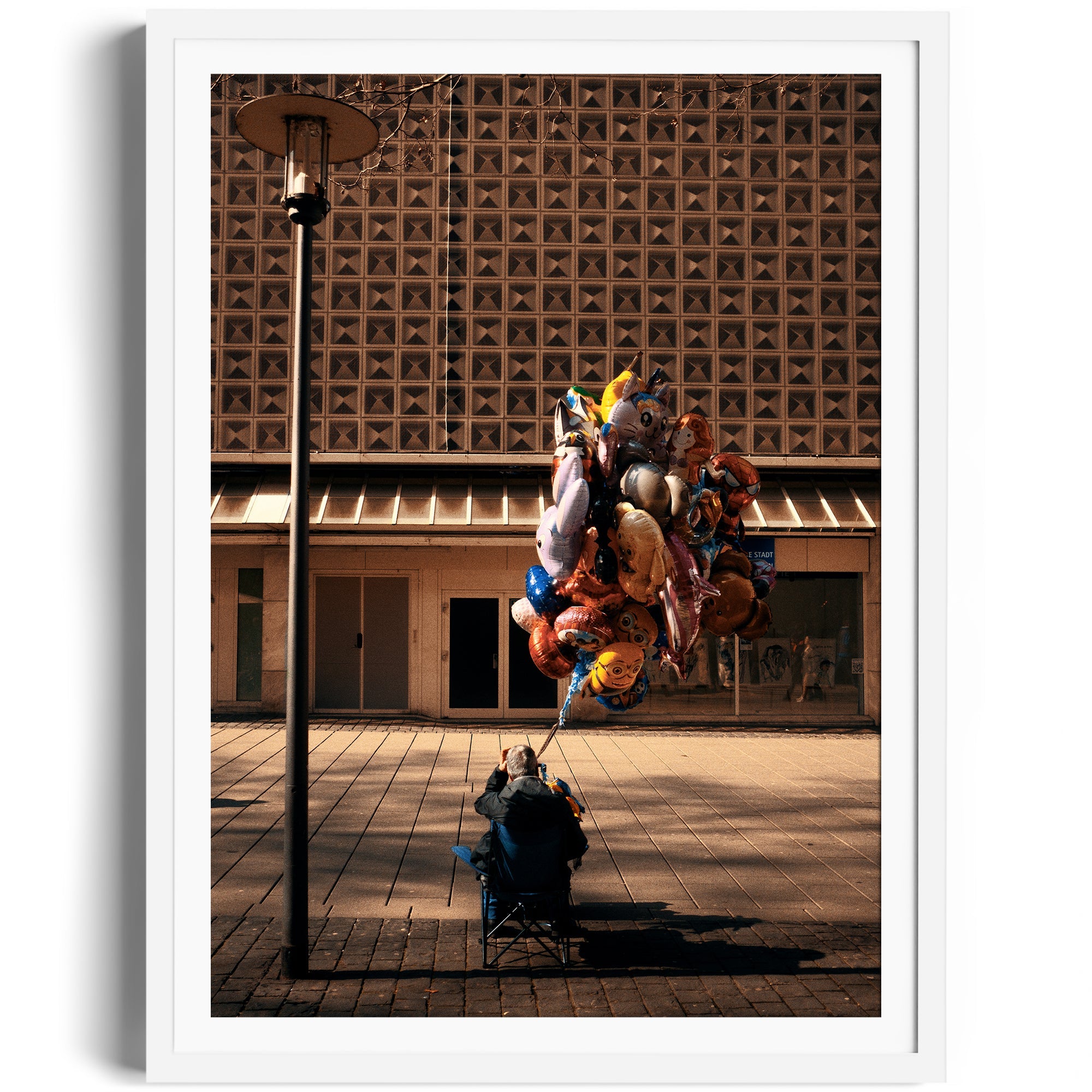 A vendor seated under a streetlamp surrounded by colorful balloons, capturing urban life in fine art photography.