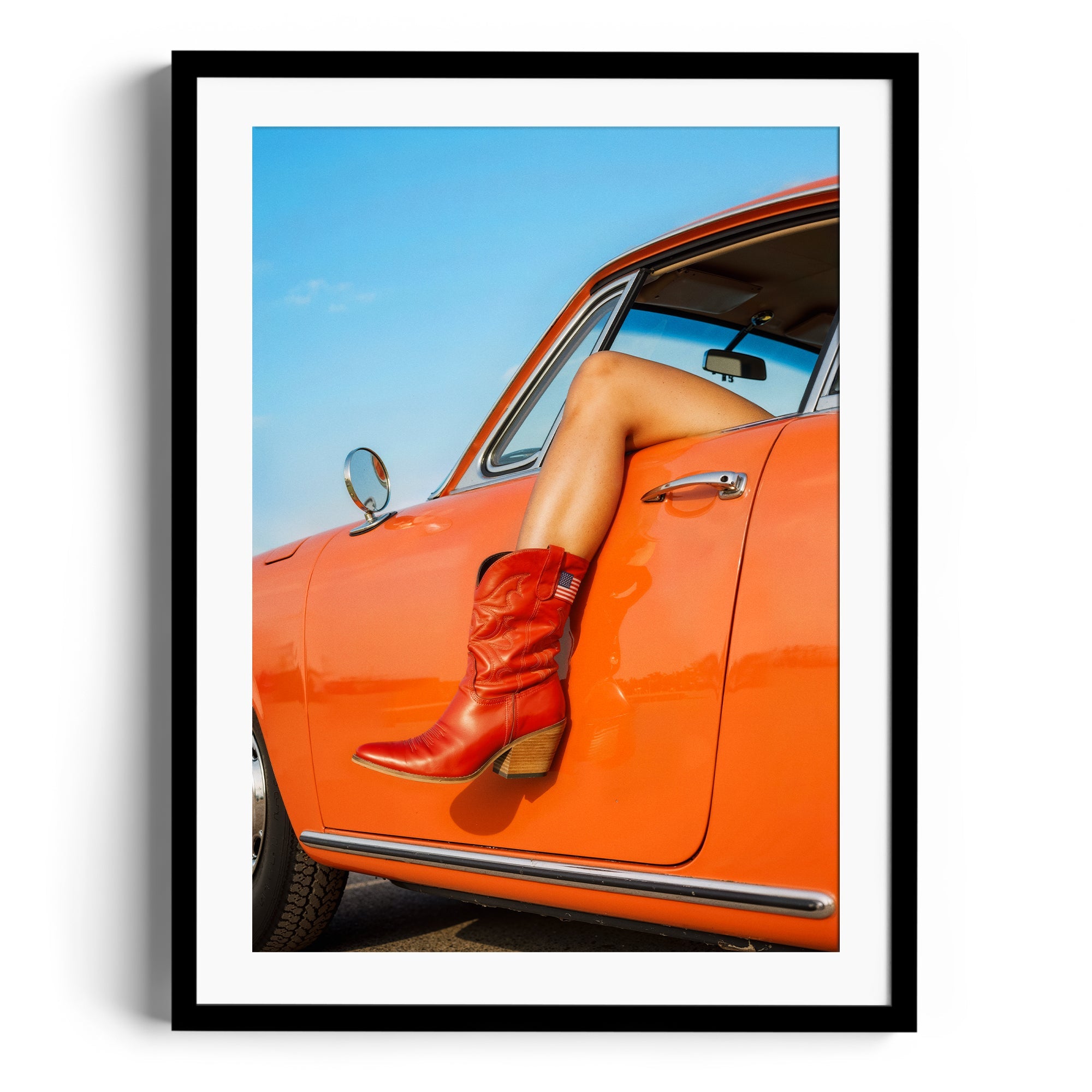 Stylish red cowgirl boots displayed in a framed art piece featuring a vibrant orange car against a clear blue sky.