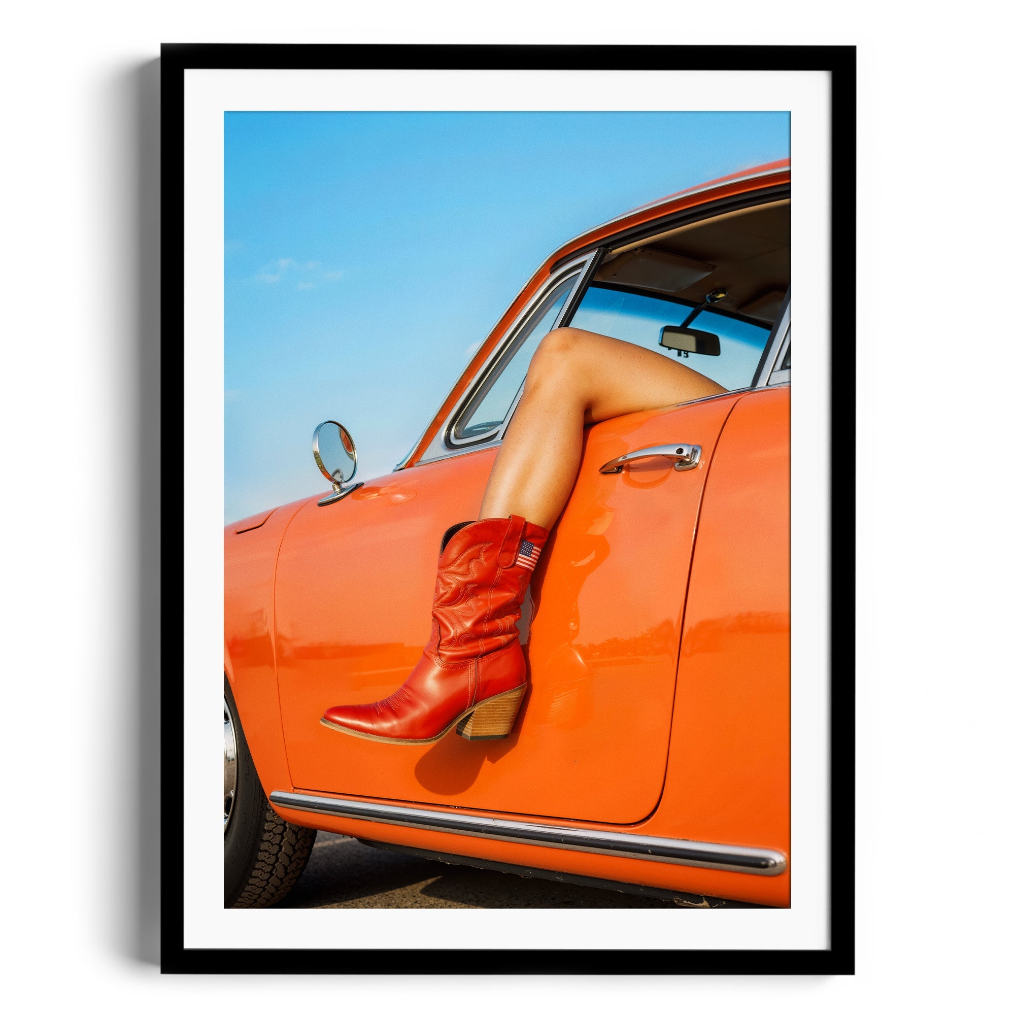 Red cowgirl boot resting on the side of an orange car against a clear blue sky, showcasing vibrant vintage style.