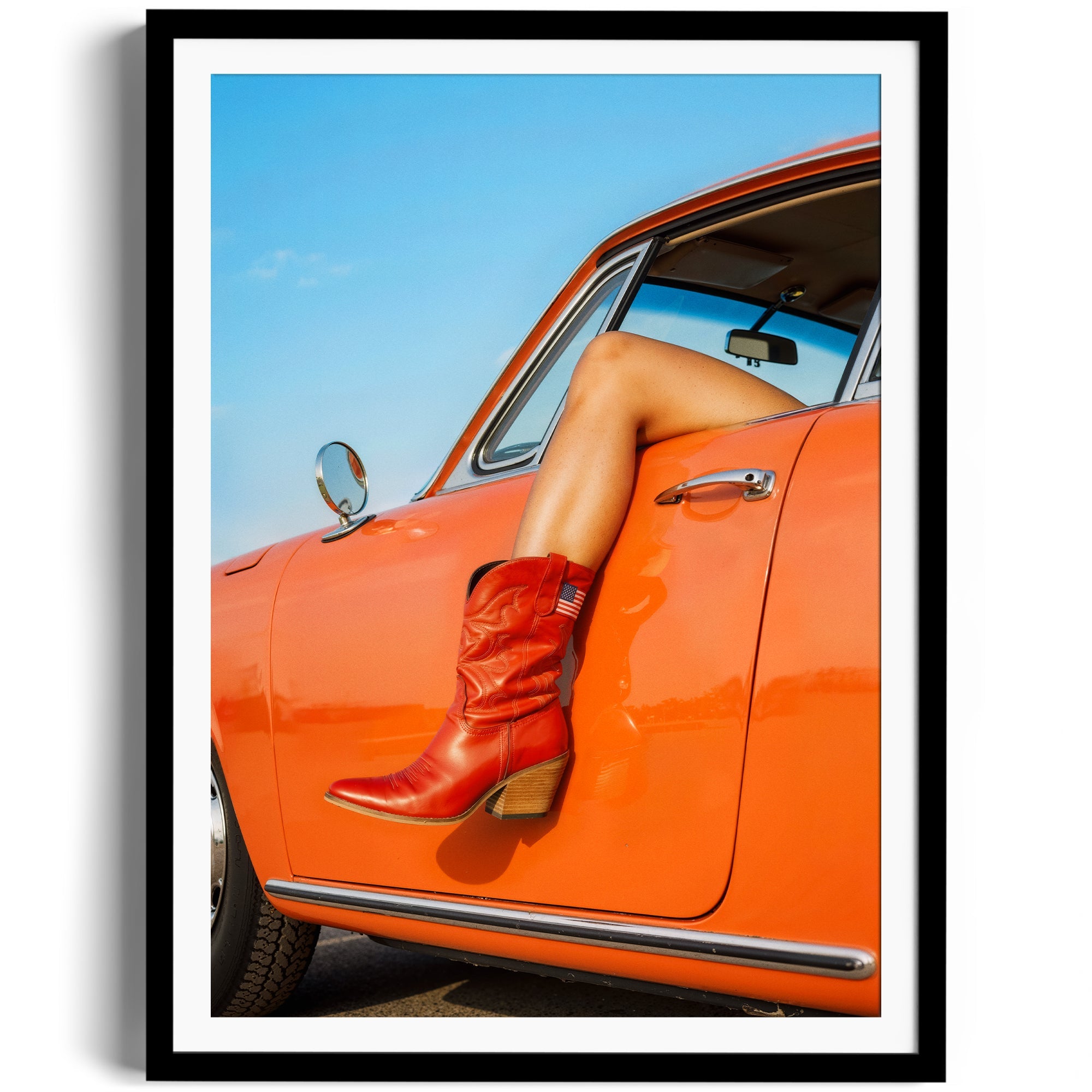 A vibrant image showcasing red cowgirl boots on a leg resting out of an orange vintage car, framed in a stylish setting.