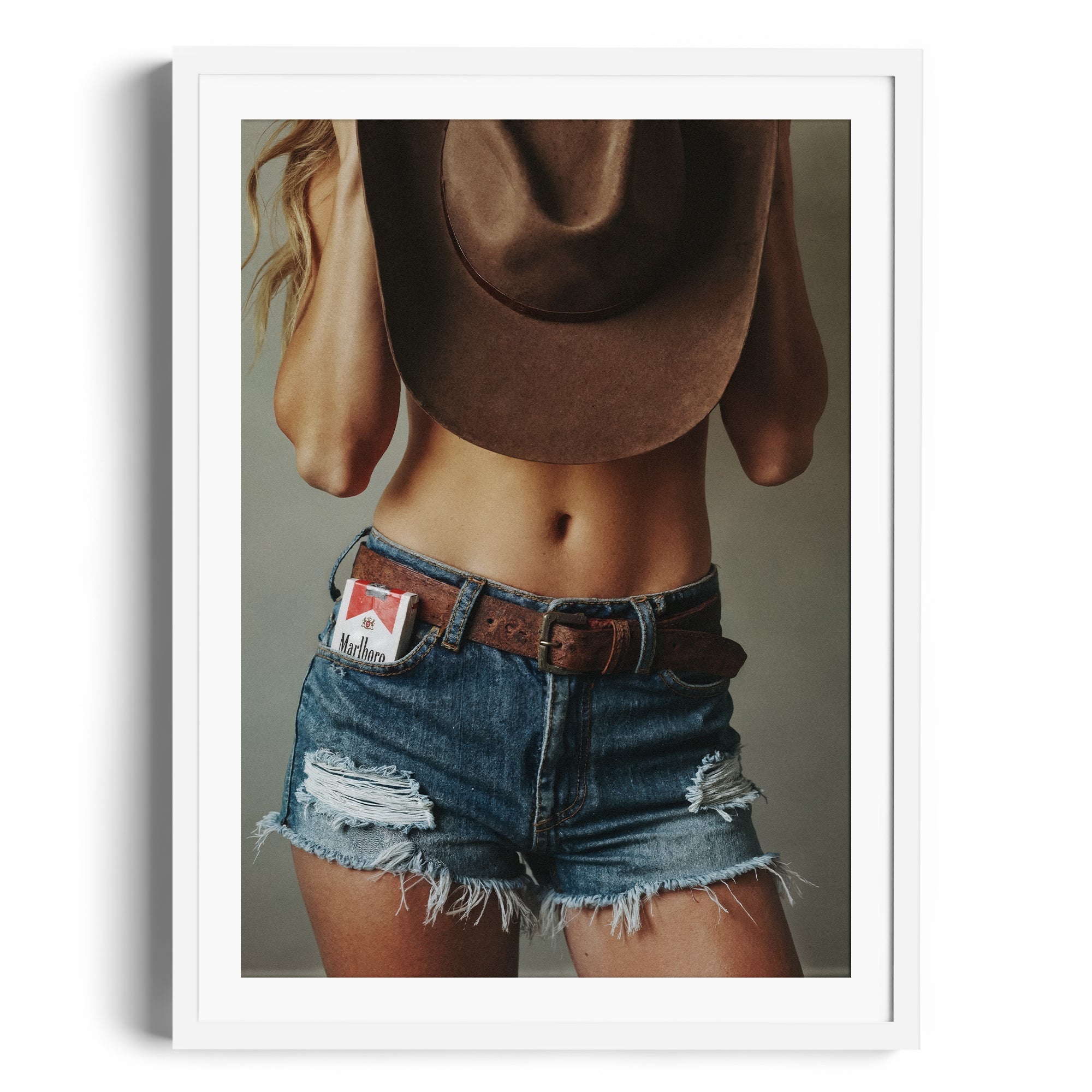 Limited Edition fine art photography of a model in denim shorts and a cowboy hat, showcasing Western allure and rebellious spirit.