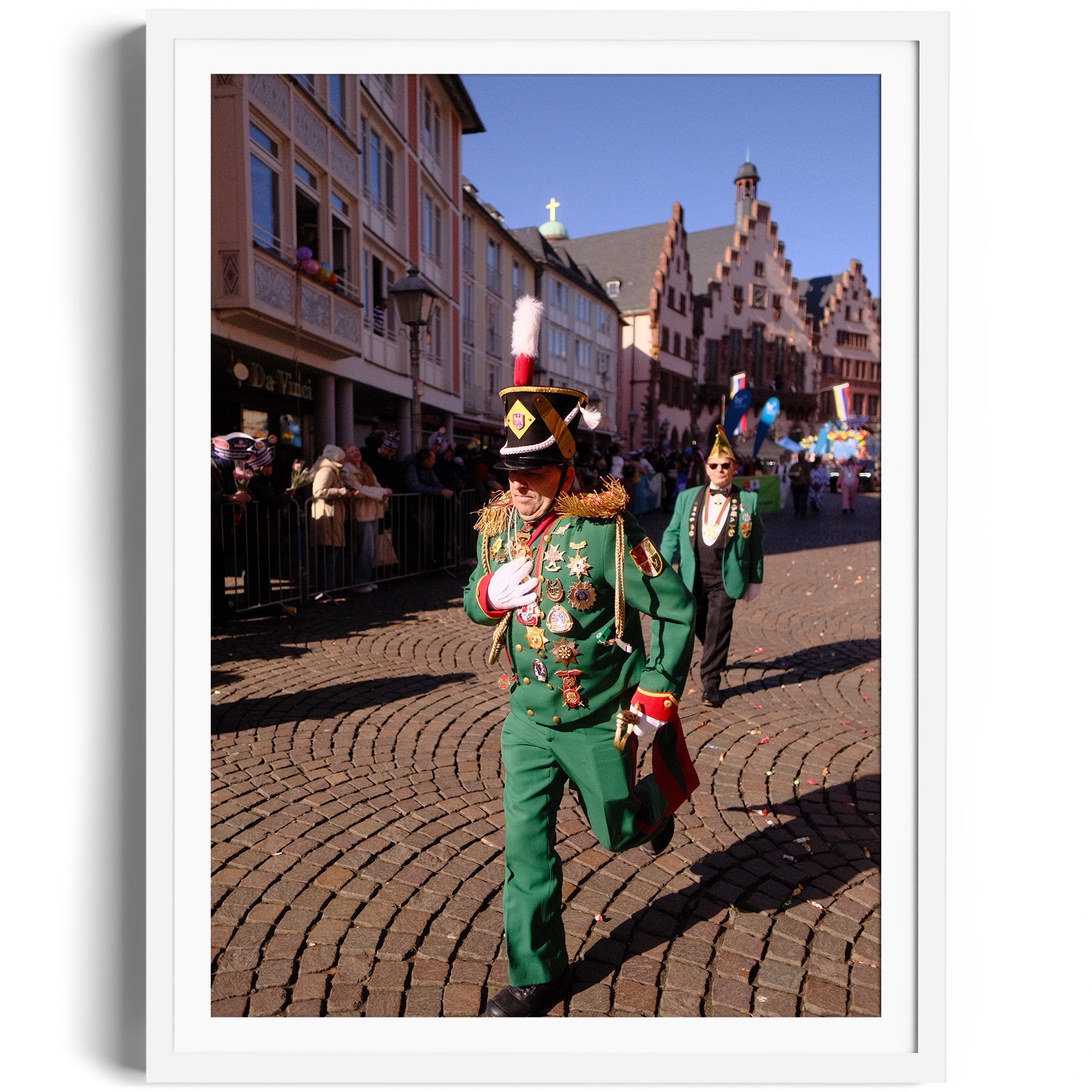 Parade scene featuring participants in green military-style uniforms at a festive event in a cobblestone street.