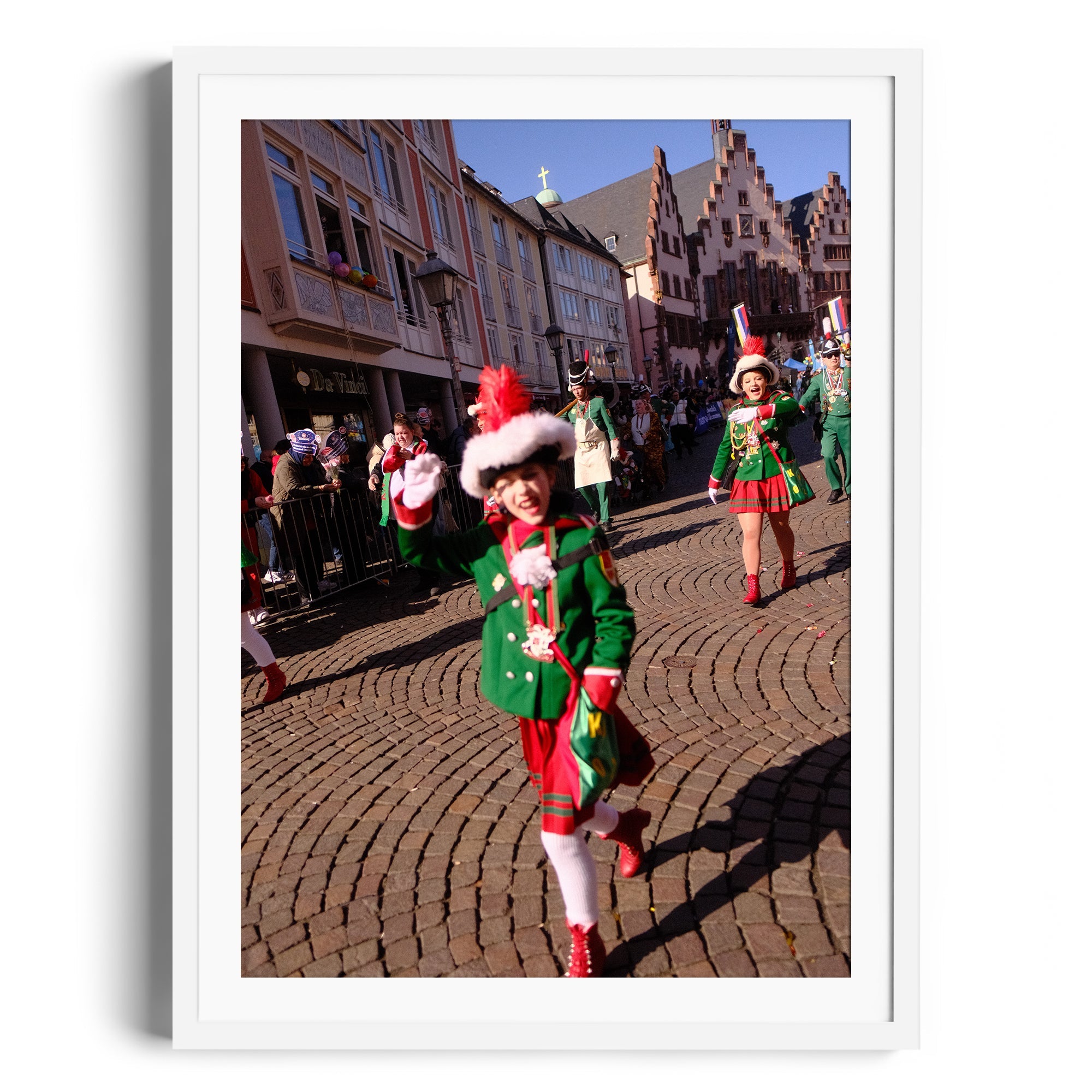 Festive parade scene with children in green outfits and hats, marching on a cobblestone street.