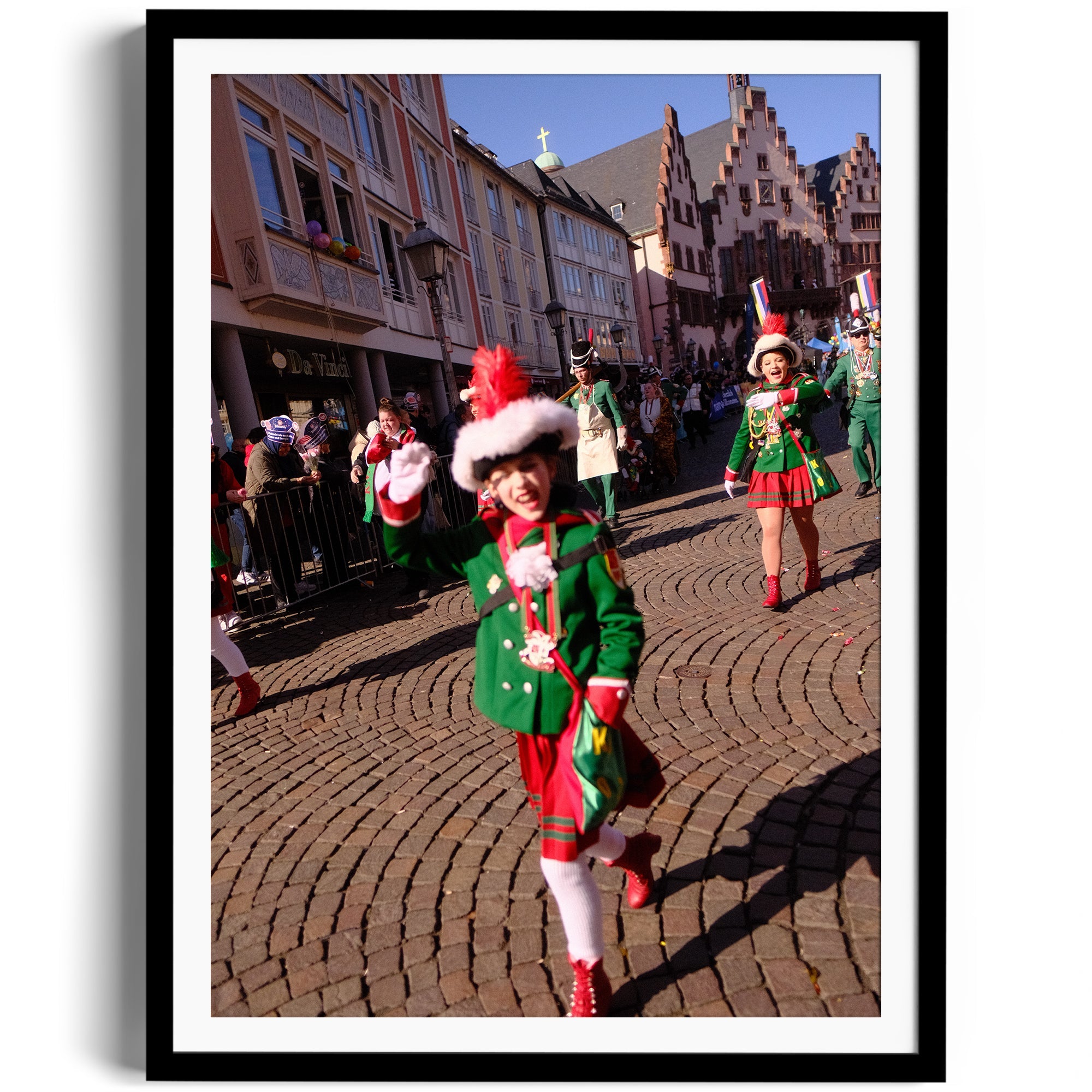 Child in festive green and red outfit dancing at a parade on cobblestone street, vibrant celebration atmosphere.
